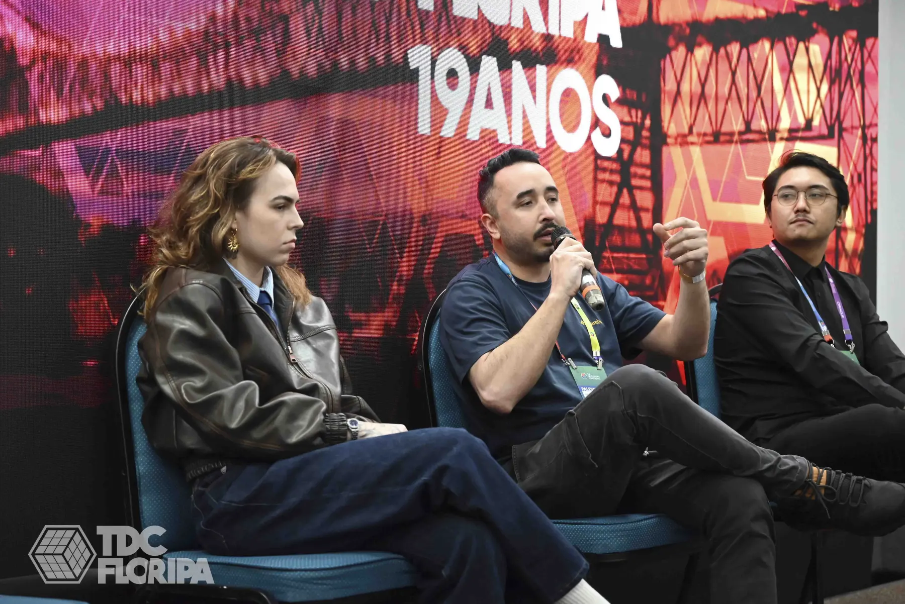 Thiago Xikota como palestrante em painel do TDC Floripa 2026, ao lado de outros dois convidados, diante do telão do evento