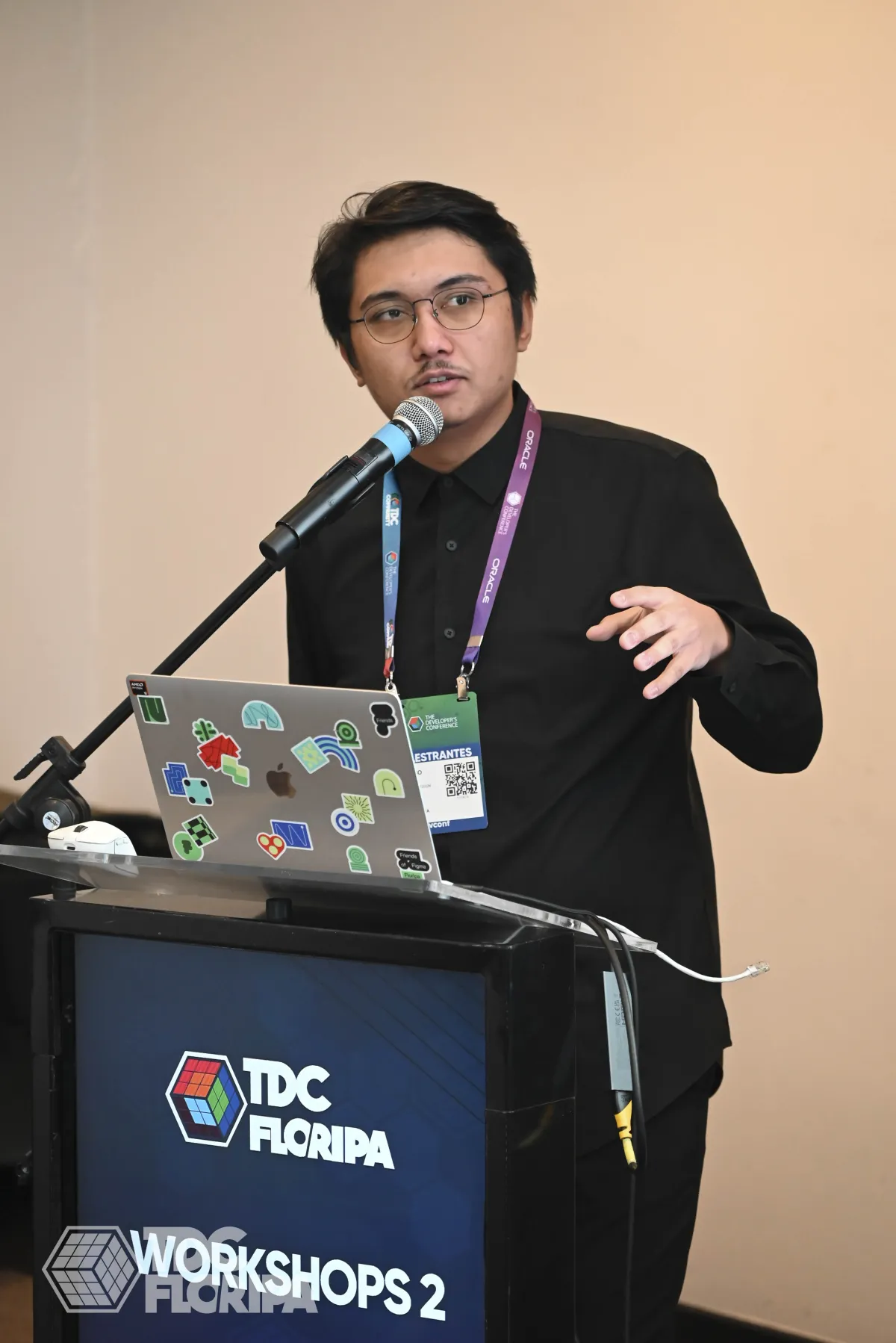 Thiago Xikota fala ao microfone no púlpito da sala de workshops do TDC Floripa 2026, com o notebook aberto à frente